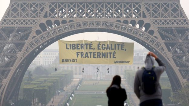 Tourists walk at Trocadero square as activists from the environmentalist group Greenpeace unfurl a giant banner on the Eiffel Tower which reads 