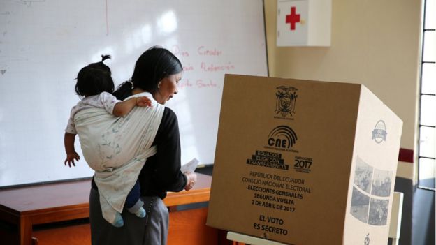 Una mujer con un niño cargado acude a votar en un centro electoral en Ecuador.