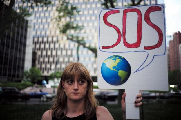 Una mujer sostiene un cartel con el planeta tierra diciendo SOS.