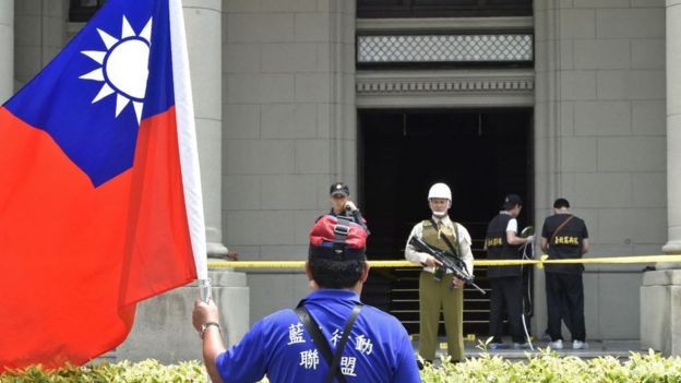 Un manifestante com uma bandeira de Taiwan em frente a um edifício oficial en Taipei