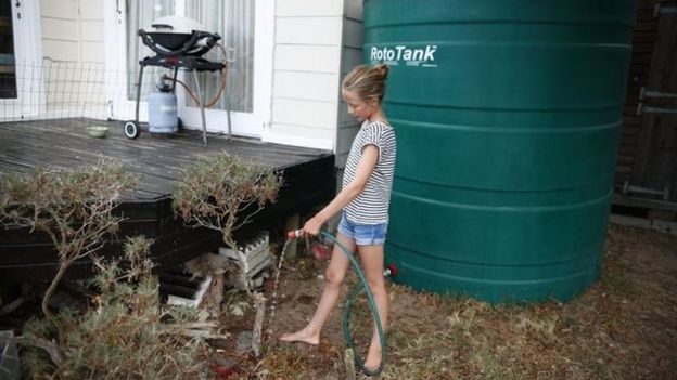 Una joven riega las plantas con agua de lluvia proveniente de un tanque en Ciudad del Cabo.