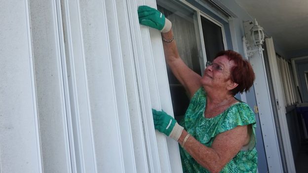 Señora poniendo contraventanas para proteger su casa