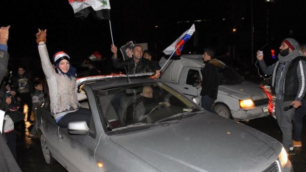 Personas celebran en Alepo con banderas sirias y rusas.