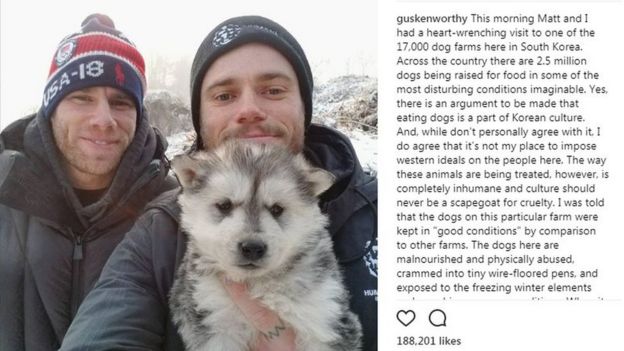 A screenshot of Gus Kenworthy's Instagram post. It contains a photo of Gus and his partner holding their dog; a puppy with long grey-and-white fur.