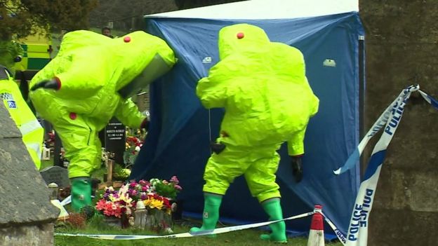 Люди в костюмах химической защиты возле могилы