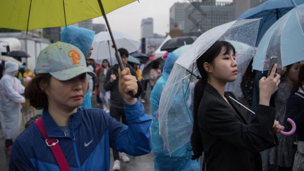 South Koreans shelter under umbrellas as they await the results of presidential election