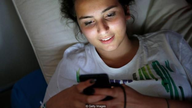 Una joven en la cama con su móvil.