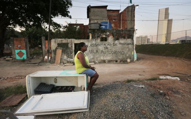 Mujer sentada sobre un refrigerador en desuso en una favela de Brasil.