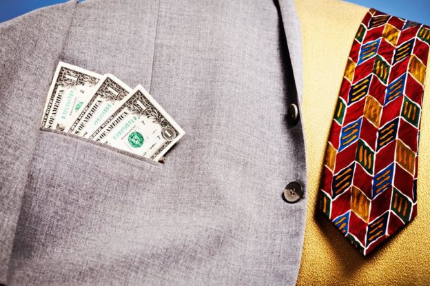 Billetes de dólar sobresalen del bolsillo de una chaqueta dejada sobre un sofá, junto a una corbata.