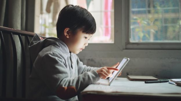 Niño asiático mirando a una tableta en una estancia interior