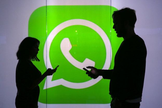 Dos personas sostienen sus celulares ante un cartel con el logotipo de WhatsApp.