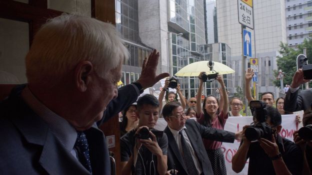 Hong Kong's former British colonial governor Chris Patten (L) waves at a small gathering of demonstrators (back, with umbrellas) as he arrives at the Foreign Correspondents' Club in Hong Kong on September 19, 2017.