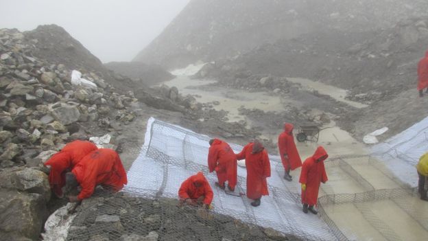 Trabajadores en Nepal colocando una malla en la ladera de una montaña para evitar el deslizamiento de rocas