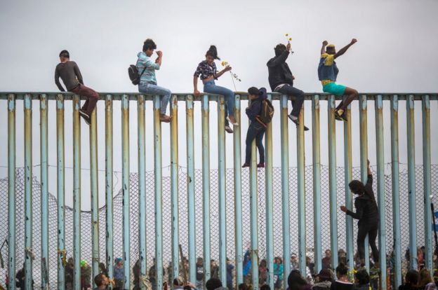 Personas sobre la reja que marca la frontera entre México y Estados Unidos