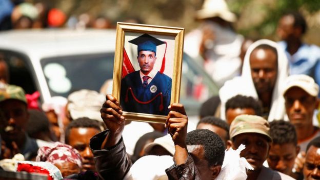 A man at a funeral holds up the portrait of Tesfu Tadese Biru in a crowd of mourners