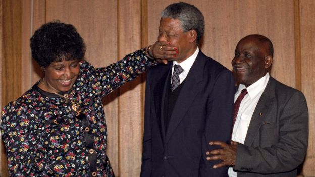 Nelson Mandela is playfully silenced by Winnie Mandela as they leave a London press conference in 1990