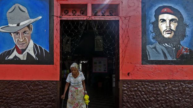 Una mujer nicaragüense camina entre un retrato de Sandino y otro del Che.