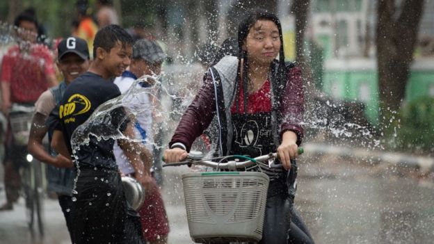 A girl cycles past revellers throwing water at passersby during celebrations marking the beginning of the Buddhist New Year