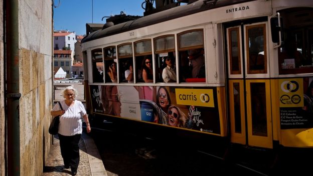 Una mujer pasea por Lisboa ante un tranvía.
