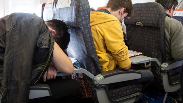 Una persona dormida sobre la mesita frente a su asiento