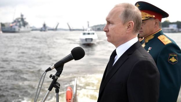 Putin junto a un militar y frente a unos barcos