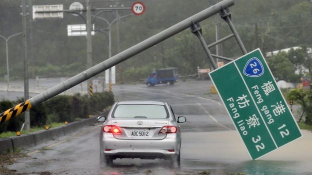 A car drives pass a collapsed traffic sign, toppled by strong winds of typhoon Meranti, as it slashes southern Taiwan on September 14, 2016.