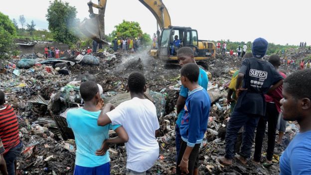 People watch rescuers search for bodies of victims buried under collapsed piles of rubbish in Maputo, Mozambique, 19 February 2018