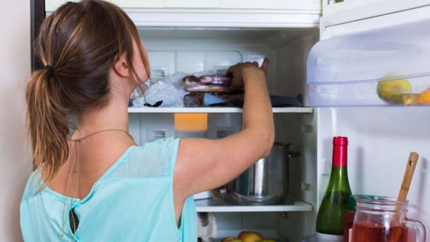 Mulher pegando comida na geladeira
