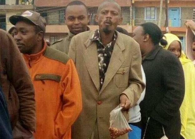 'GitheriMan' akisimama kwenye foleni akishika mfuko wa plastiki