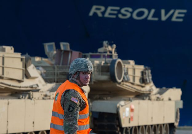 A US soldier walks in front of US Army tanks and the cargo vessel 