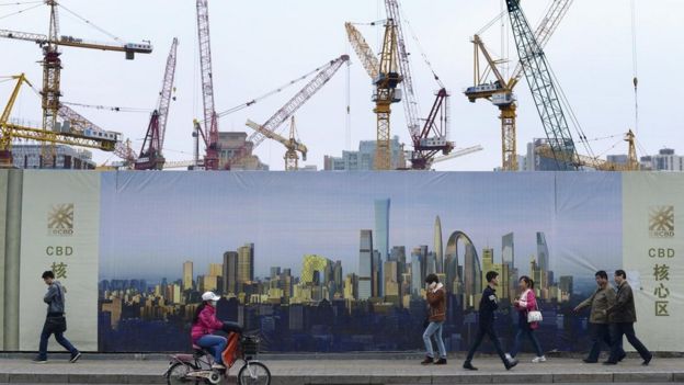 Personas caminando y pedaleando frente a una construcción.