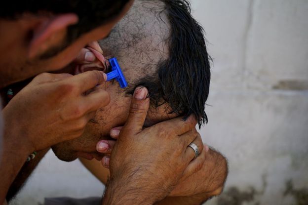 Un migrante le corta el pelo a otro en una fábrica abandonada en Serbia.