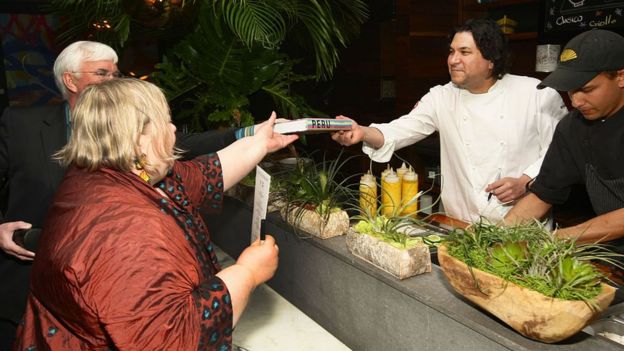 El chef peruano Gastón Acurio alcanza un libro a una pareja.