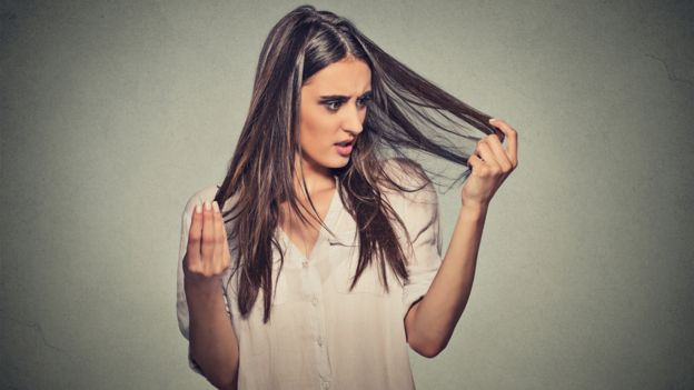 Una mujer parada se agarra las puntas del cabello