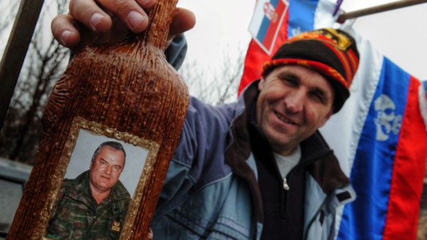 Hombre mostrando una botella de brandy que tiene la imagen de Ratko Mladic