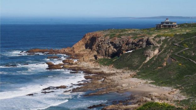 A jagged coastline by the sea. Tarpaulin is just visible behind a ridge, indicating the location of the dig site