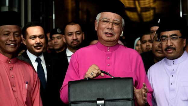Najib Razak poses with his briefcase as he leaves to unveil the 2017 financial budget