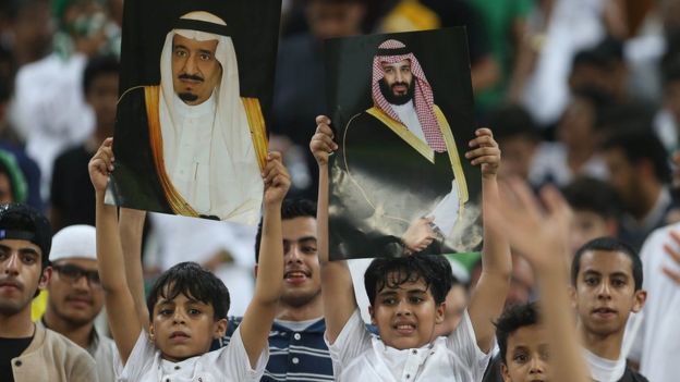 Seguidores de la selección de fútbol de Arabia Saudita sostienen fotos de la familia real durante un partido.