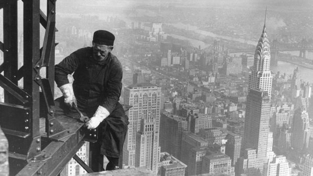 Un obrero trabaja desde las alturas en la construcción del Empire State, con el edificio Chrysler de fondo.