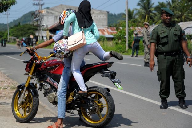 Endonezya'da yasağa uymayarak hem motorsiklete normal pozisyonunda binen hem de dar pantolon giyen bir kadın Şeriat Polisi tarafından durdurulurken