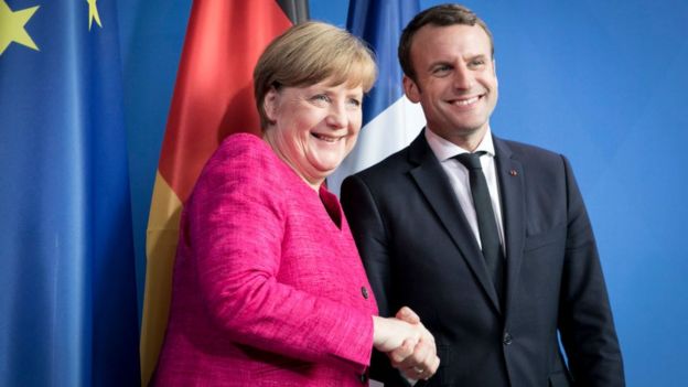 Angela Merkel y Emmanuel Macron dándose la mano.