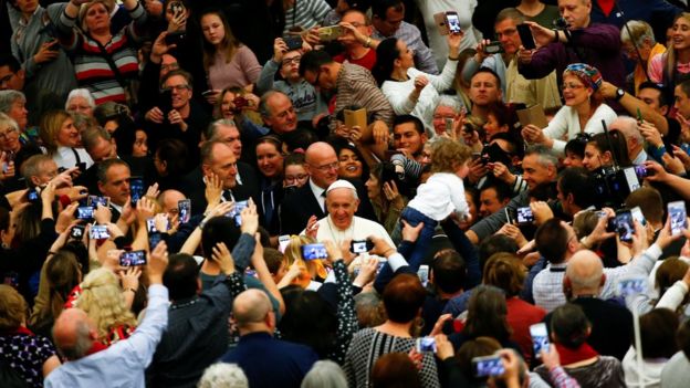 O papa Francisco em meio a uma multidão de fiéis com câmeras e celulares