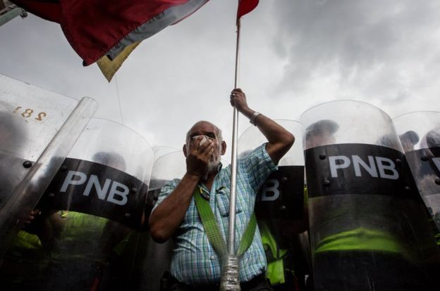 Anciano con una bandera venezolana frente a policías