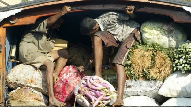 Two men ride on back of open truck, whilst holding in food produce for sale at market stall in Colombo. File photo