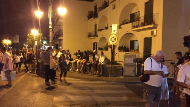 people are pictured sitting on walls and checking phones for information in the street