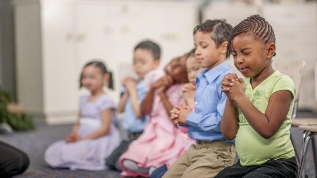 Crianças rezando em sala de aula