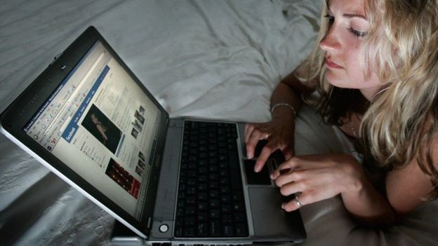 Mulher olha página do Facebook em um notebook