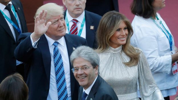 Donald Trump waves as he stands in Sicily next to his wife Melania