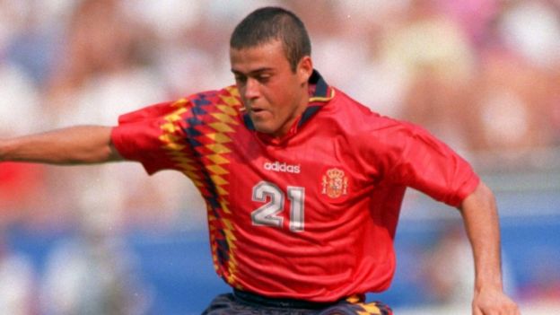 LuisEnrique concentrates on his run, arms in the airs, at the 1994 World Cup. He's wearing a red shirt, number 21, with diamonds on the right-hand side.