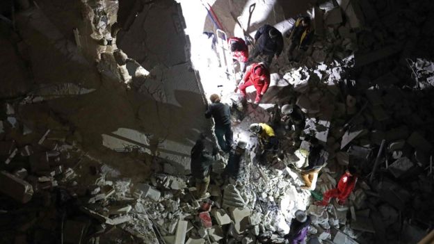 Rescue workers search for survivors in the remains of a block of flats destroyed in a reported air strike in Idlib city (4 February 2018)